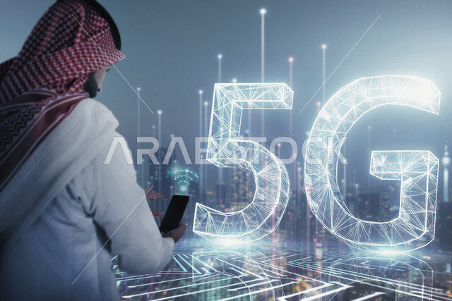 صورة مقربة من الخلف لرجل عربي خليجي سعودي بيده موبايل أمام اختصار الجيل الخامس للشبكات 5G و أبراج المملكة بتقنية الهولوجرام ، استخدام خاصية الهولوجرام ثلاثية الأبعاد .