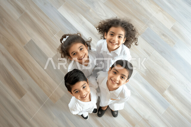 مفهوم التعلم في المملكة العربية السعودية، التعليم والتربية بالمناهج المقررة للطلاب، استقبال العام الدراسي الجديد بحماس، صورة علوية عامودية لمجموعة تلاميذ عرب خليجيين سعوديين مبتسمين يتظرون الى الكاميرا بتعابير السرور والسعادة