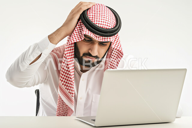 الشعور بالانزعاج والصدمة, الخسارة والفشل في تحقيق الأهداف, تعابير الاندهاش بسماع الاخبار السيئة, بورتريه  مقرب لرجل عربي سعودي خليجي يرتدي الشماغ والثوب التقليدي يضع يديه على رأسه بإيماءات الذهول يقوم باستخدام جهاز الحاسوب المحمول