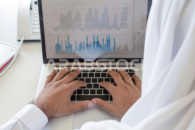 مفهوم العمل عن بعد، استخدام الاجهزة التقنية الحديثة، ادارة مهام العمل اليومية في مقر الشركة، صورة مقربة لرجل عربي خليجي سعودي يرتدي الزي التقليدي يجلس في مكتبه يعمل على جهاز الحاسوب المحمول، مهن ووظائف سعودية