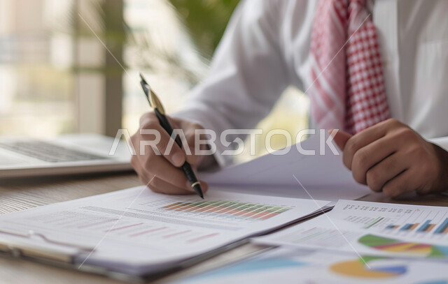 مفهوم الدقة والتركيز في انجاز المعاملات، تحقيق الاهداف المالية للشركة، صورة مقربة لرجل أعمال عربي خليجي سعودي يقوم بدراسة الأرباح، جمع بيانات البورصه وسوق الأسهم, دراسة و تحليل الاحصائيات و الرسوم البيانية, دمج التكنولوجيا مع العمل.