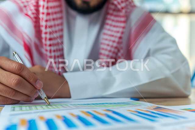 The concept of accuracy and focus in completing transactions, achieving the company's financial goals, a close-up image of a Saudi Arabian Gulf businessman studying profits, collecting stock market and stock exchange data, studying and analyzing statistics and charts, integrating technology with work.