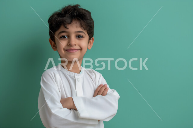 التقاط صور شخصية للوثائق الرسمية، النظر الى الكاميرا بايماءات السعادة والثقة بالنفس، ملامح طفولية بريئة، الأناقه والاهتمام بالمظهر الخارجي، بورتريه مقرب لولد عربي سعودي خليجي مبتسم يرتدي الزي التقليدي يقف بأيدي متقاطعة، خلفية حضراء