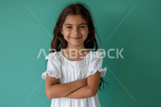 الوقوف باستقامة بأيدي متقاطعة بتعابير الثقة بالنفس، ملامح طفولية بريئة، الأناقه والاهتمام بالمظهر الخارجي، بورتريه مقرب لفتاة عربية سعودية خليجية مبتسمة ترتدي فستان أبيض تنظر الى الكاميرا بايماءات السعادة والبشاشة، التقاط صور شخصية للوثائق الرسمية، خلفية خضراء