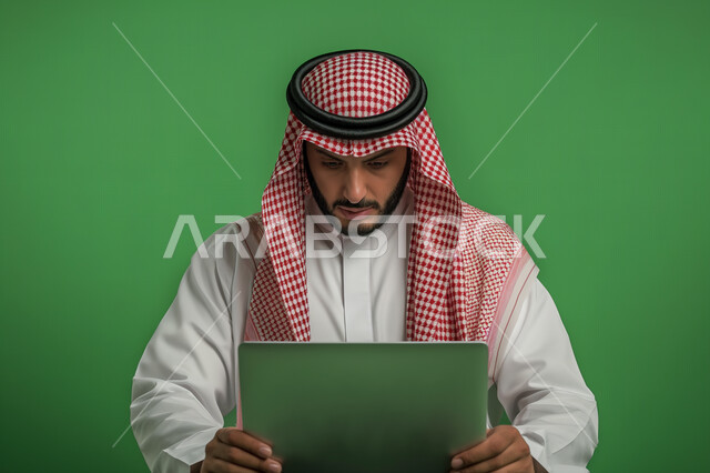 استخدام الأجهزة والتقنيات الحديثة لتسهيل الأعمال, إجراء مقابلات عمل أونلاين, مهن ووظائف سعودية مكتبية، بورتريه مقرب لرجل أعمال عربي سعودي خليجي يرتدي الزي التقليدي والشماغ يجلس على مكتب أمام  جهاز الحاسوب المحمول، ايماءات وتعابير التركيز والاندماج,خلفية خضراء