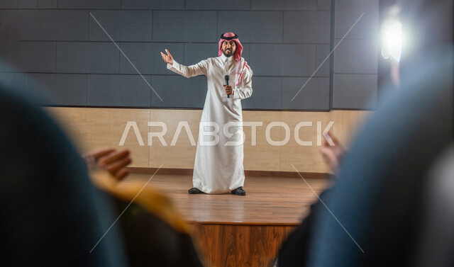 مقدم مسرحي سعودي خليجي على خشبة المسرح يتفاعل مع الجمهور ،  تقديم العروضات المسرحية ، القاء الخطابات ، الحوارات و النقاشات ، اداء تمثيلي ، ايماءات وجه و يدين مختلفة ، الفن المسرحي 