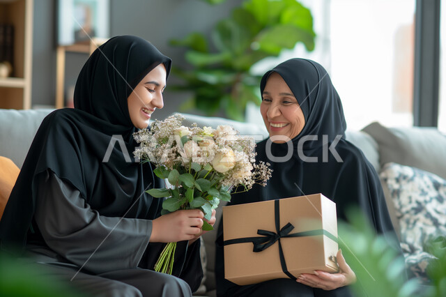تقديم الهدايا في الأعياد والمناسبات، إيماءات الرضا والسعادة، إحياء ذكرى عيد الأم، مفهوم احترام وتقدير الوالدين، شابة عربية خليجية سعودية محجبة تقوم بإهداء أمها باقة من الزهور وعلبة هدية مغلفة بشكل أنيق، إدخال السرور إلى قلب الأهل، تماسك الأسرة السعودية