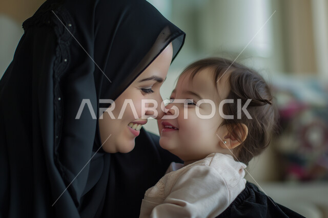 الشعور بالأمان والاطمئنان، تعزيز رابط الأمومة بين الأم وصغيرتها، إيماءات السعادة والسرور، مفهوم حنان الأمهات و تحمل المسؤولية والعناية بالأطفال، سيدة عربية خليجية سعودية محجبة تحضتن طفلتها وتنظر إليها بحب وتقوم بمداعبتها، قضاء الأوقات الممتعة مع الأبناء