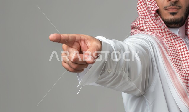 الاشارة إلى شيء ما بأصبع السبابة, اشارات التأكد والاستغراب, بورتريه لرجل عربي خليجي سعودي يرتدي الثوب التقليدي والشماغ يرفع إصبعه للتحديد والاختيار, الدلالة نحو هدف ما، خلفية رمادية