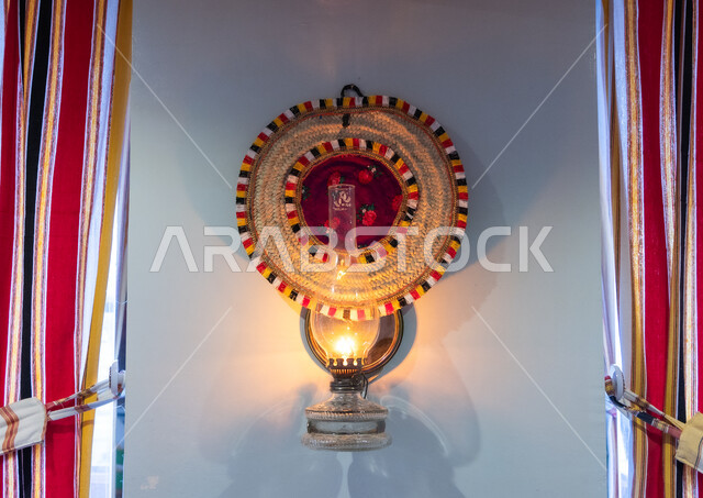 الفانوس الزجاجي المتوهج المعلق على حائط في إحدى المباني التراثية, استخدام سعائف الخوص في الصناعة المنزلية, الأصالة والتراث السعودي. أدوات قديمة بطابع شعبي قديم في المملكة العربية السعودية