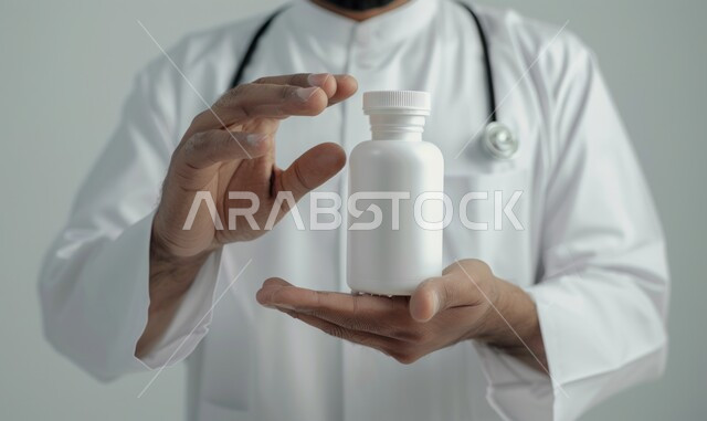 استخدام العلاج الطبي اللازم, تقديم الخدمات الطبية للمرضى, بورتريه مقرب لطبيب عربي خليجي سعودي يرتدي المعطف الابيض وسماعة الفحص يمسك بيده علبة الدواء, أدوية لمعالجة الحالات المرضية, الوقاية من الأمراض والعدوى، خلفية بيضاء