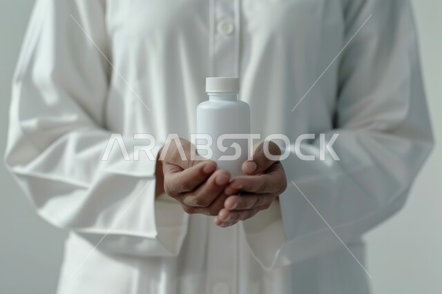 الوقاية من الأمراض والعدوى، تقديم الخدمات الطبية للمرضى, صورة مقربة لطبيب عربي خليجي سعودي يرتدي المعطف الابيض و يمسك بيده علبة الدواء, أدوية لمعالجة الحالات المرضية, استخدام العلاج الطبي اللازم