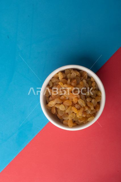 الزبيب (العنب المجفف) نوع من أنواع الفواكهة المجففة , صورة مقربة للزبيب المجفف , فواكة مجففة صحية ولذيذة , عنصر غذائي مفيد للصحة , خلفية ملونة بالأزرق والزهري