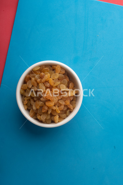الزبيب (العنب المجفف) نوع من أنواع الفواكهة المجففة , صورة مقربة للزبيب المجفف , فواكة مجففة صحية ولذيذة , عنصر غذائي مفيد للصحة , خلفية ملونة بالأزرق والزهري