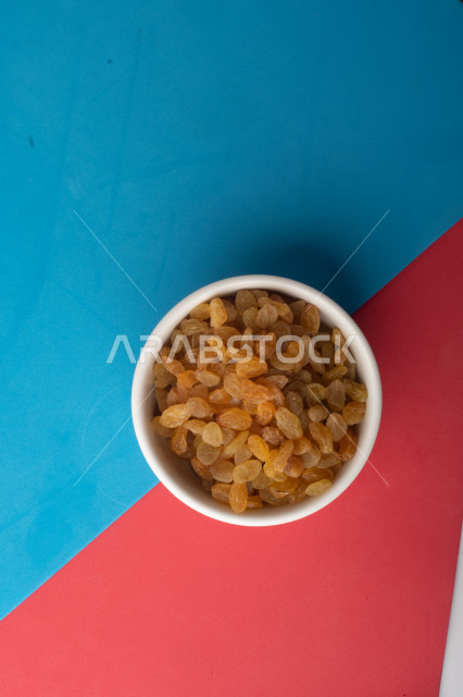 الزبيب (العنب المجفف) نوع من أنواع الفواكهة المجففة , صورة مقربة للزبيب المجفف , فواكة مجففة صحية ولذيذة , عنصر غذائي مفيد للصحة , خلفية ملونة بالأزرق والزهري