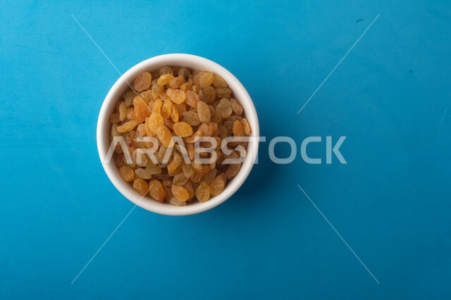 الزبيب (العنب المجفف) نوع من أنواع الفواكهة المجففة , صورة مقربة للزبيب المجفف , فواكة مجففة صحية ولذيذة , عنصر غذائي مفيد للصحة, خلفية ملونة باللون الأزرق