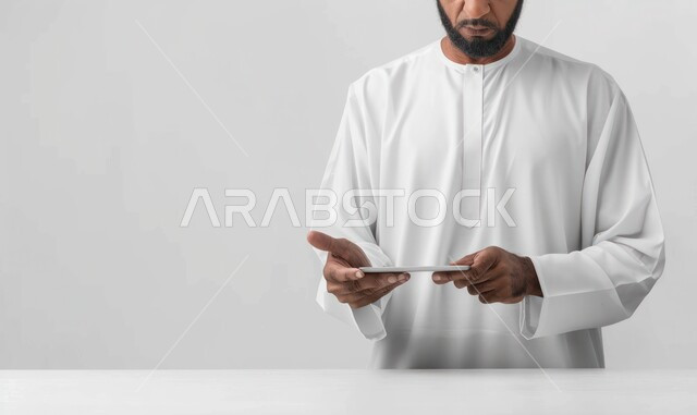 التسويق الإلكتروني عبر الأجهزة الحديثة، متابعه آخر أخبار السوشال ميديا،  تصفح مواقع التواصل الإجتماعي، البحث عن عمل عن طريق الانترنت، بورتريه مقربة لرجل عربي خليجي سعودي يرتدي الزي التقليدي يحمل بيده جهاز التابليت، خلفية بيضاء