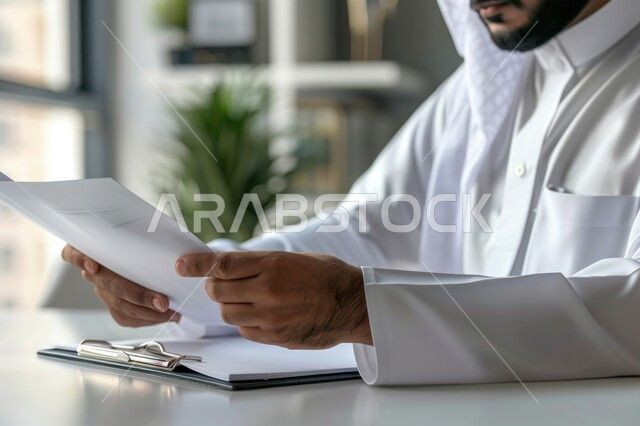 Following up on work reports and tasks, comparing plans and projects with implementation, a Saudi Gulf businessman wearing traditional clothing carrying a set of papers and bonds, commercial office jobs and professions, auditing the results of meetings and seminars