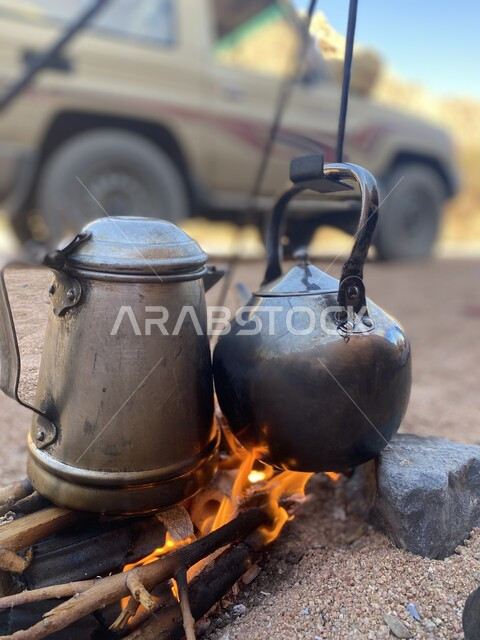 ابريق الشاي الفضي المعدني على نيران الحطب، اعداد الشاي على النيران المشتعلة في الطبيعة، اللهب الاصفرالمشتعل
