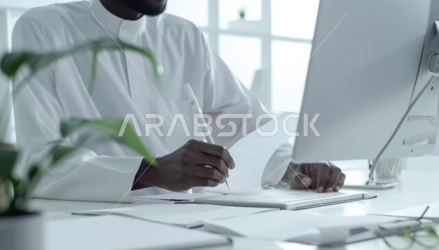 مهن وأعمال مكتبية تجارية، استخدام الأجهزة والتقنيات الحديثة لإنجاز المهام، رجل أعمال سعودي خليجي يرتدي الزي التقليدي يعمل على جهاز الحاسوب المحمول، مفهوم إدارة الأعمال، عقد صفقات عمل عبر الإنترنت، مراجعة ومتابعة البحوث العلمية وخطة العمل في مقر الشركة