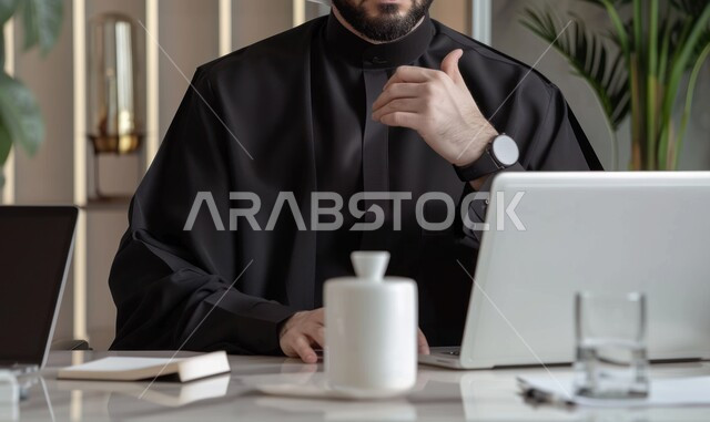 تحقيق الاهداف المالية للشركة، مفهوم الدقة والتركيز في انجاز المعاملات، مفهوم إدارة شؤون الأعمال وتنظيمها عبر الاجهزة التقنية, دمج العمل مع التكنولوجيا الحديثة، صورة مقربة لرجل أعمال عربي خليجي سعودي يرتدي الزي التقليدي الأسود يقوم بمراجعة المستندات في مكتبه