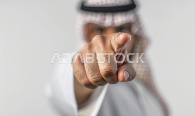 النظر الكاميرا بتعابير العصبية والغضب، الاشارة إلى شيء ما، بورتريه لرجل عربي خليجي سعودي يرتدي الزي التقليدي والشماغ يشير بأصبع السبابة لتوجيه الاتهام، ايماءات التحذير والتنبيه, التحديد والتأكيد والاختيار، خلفية بيضاء