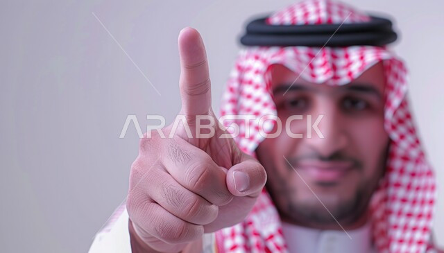 Identify, confirm and select, looking at the camera with nervous and angry expressions, pointing at something, portrait of a Saudi Arabian Gulf man wearing traditional dress and a shemagh pointing with his index finger to accuse, warning and alert gestures, white background