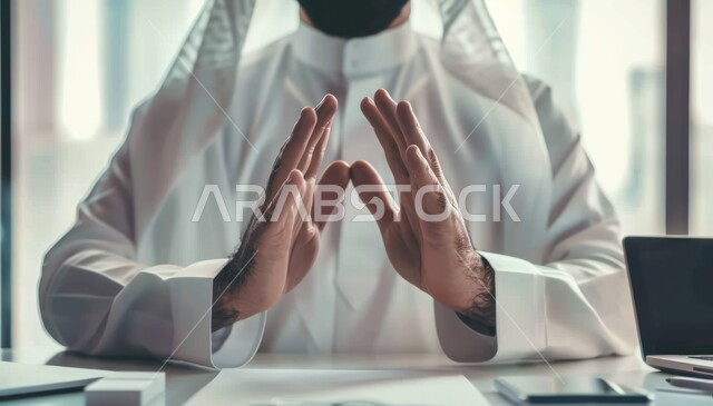 القلق والاحتياط والابتعاد عن شيء ما ، مهن ووظائف مكتبية سعودية، رجل عربي سعودي خليجي يرتدي الزي التقليدي يجلس على المكتب الحديث، رفع اليدين بايماءات تدل على إشارة الحماية وعدم الاقتراب