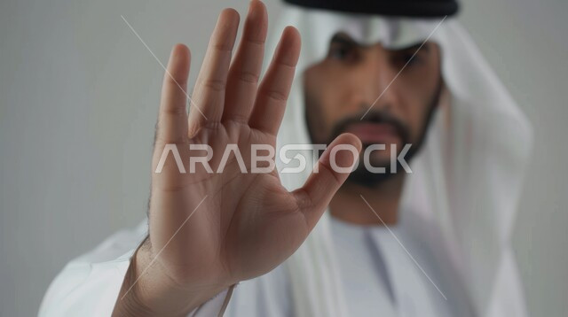 الصمت والتوقف عن الكلام, الامتناع عن فعل أمر معين, بورتريه مقرب لرجل عربي خليجي سعودي يرتدي الغترة والعقال يرفع كفه للأعلى بإيماءات طلب عدم التدخل وخفض الصوت والتهديد, الوقوف بانزعاج ورفض أمر محدد, خلفية رمادية