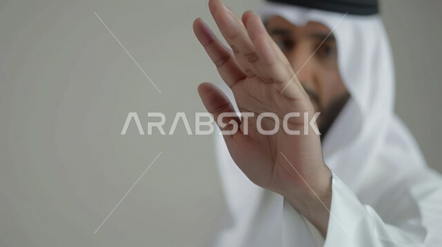 الامتناع عن فعل أمر معين, بورتريه مقرب لرجل عربي خليجي سعودي يرتدي الغترة والعقال يرفع كفه للأعلى بإيماءات طلب عدم التدخل وخفض الصوت والتهديد, الوقوف بانزعاج ورفض أمر محدد, الصمت والتوقف عن الكلام, خلفية رمادية