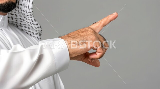 تحديد هدف ما والاشارة نحو شيء، بورتريه مقرب ليد رجل عربي خليجي سعودي يرتدي الثوب التقليدي والشماغ يشير بأصبع السبابة على مكان معين, خلفية رمادية