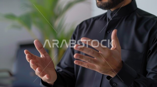 اعطاء الندوات والمحاضرات بإيماءات التفاعل والاندماج, تقديم الافكار والمعلومات, صورة مقربة لرجل عربي خليجي سعودي يرتدي الزي الكاجوال يقوم بالمناقشة والحوار, نباتات الزينة المكتبية