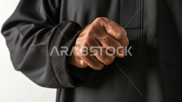 محاولة ضبط الأعصاب, القوة والقدرة على فعل شيء ما, تعابير الغضب والانزعاج والتحدي, بورتريه مقرب ليد رجل عربي خليجي سعودي يرتدي الثوب التقليدي يرفع قبضة يده بانفعال, خلفية بيضاء