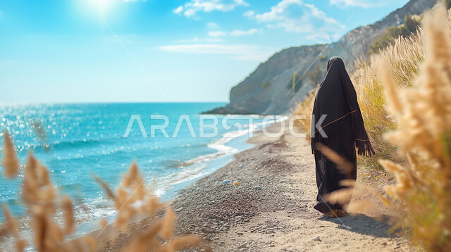 Trips to coastal areas, enjoying the summer atmosphere, a picture from behind of a veiled Saudi Gulf Arab woman wearing a black abaya walking on the seashore, blue skies on the beaches