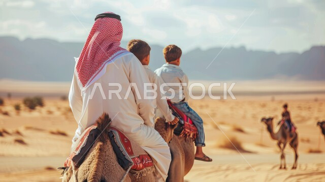 الاهتمام والعناية بالثدييات في المناطق الصحراوية، صورة من الخلف لرجل عربي خليجي سعودي يرتدي الشماغ والثوب التقليدي يركب الإبل مع ولده في الصحراء، تربية الجمال في المحميات الطبيعية، المناظر الطبيعية والرمال الذهبية الناعمة في صحاري المملكة العربية السعودية