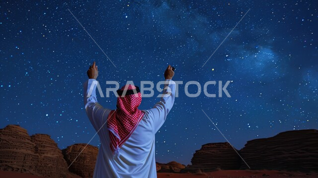 Rock formations and formations, a picture from the back of a Saudi Arabian Gulf man wearing a traditional shemagh and thobe raising his hands up watching the Milky Way in the sky of AlUla Governorate, famous tourist places and landmarks in the Kingdom of Saudi Arabia
