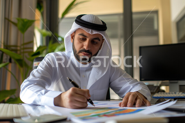 The concept of accuracy and focus in completing transactions, achieving the company's financial goals, a close-up image of a Saudi Arabian Gulf businessman studying profits, collecting stock market and stock exchange data, studying and analyzing statistics and charts, integrating technology with work.