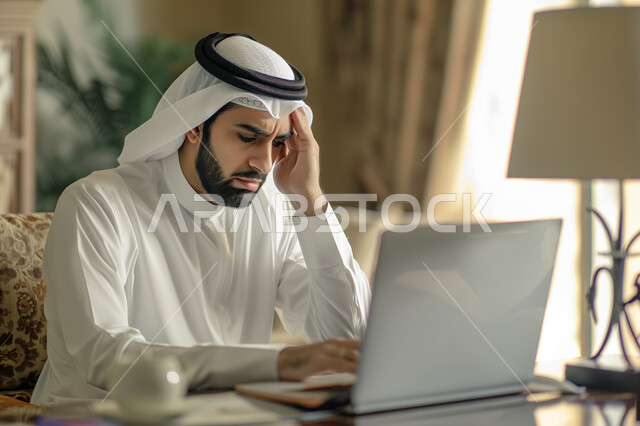 مفهوم ضغط العمل, تعابير الحزن والتعب, وظائف ومهن مكتبية, إيماءات الصداع والضجر, صورة مقربة لرجل عربي خليجي سعودي يرتدي الشماغ والثوب التقليدي يضع يديه على رأسه يقوم باستخدام الحاسب المحمول, إدارة وتنظيم الأعمال ضمن مقر الشركة