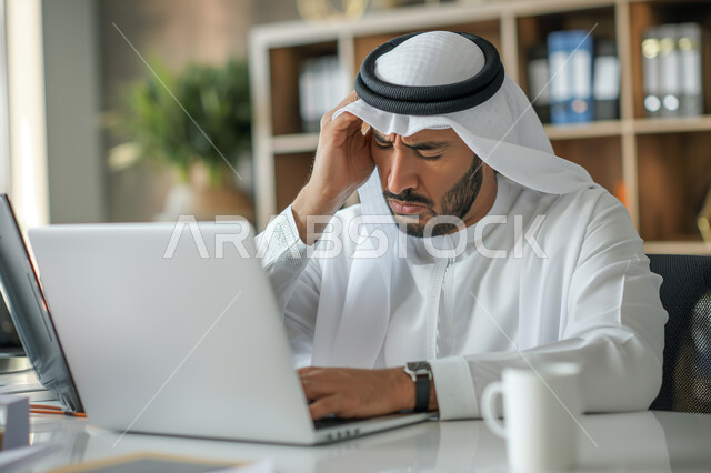 Work pressure concept, expressions of sadness and fatigue, office jobs and professions, gestures of headache and boredom, close-up of a Saudi Arabian Gulf man wearing a traditional shemagh and thobe with his hands on his head using a laptop, business management and organization within the company's headquarters