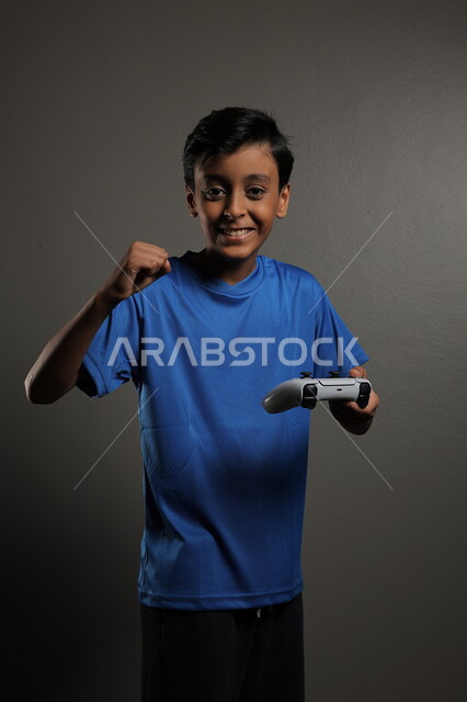 Having fun playing at home, using modern technology for entertainment and fun, portrait of a Saudi Arabian Gulf boy wearing casual clothes playing video games with gestures of integration and focus, gray background