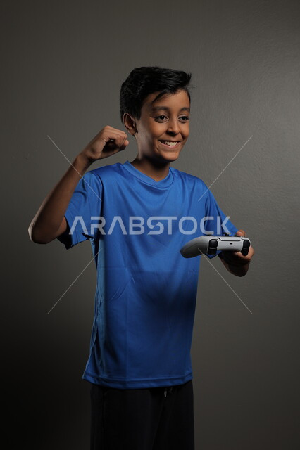 Using modern technologies for entertainment and fun, spending fun times playing at home, portrait of a Saudi Arabian Gulf boy wearing casual clothes playing video games with gestures of integration and focus, gray background
