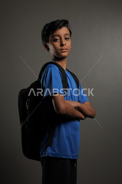 الإستعداد للعام  الجديد، الوقوف باستقامة بايماءات السعادة للعودة إلى المدارس ,  بورتريه لطالب عربي خليجي سعودي يرتدي الزي الكاجوال و يحمل الحقيبة المدرسية وينظر إلى الكاميرا ، الشعور بالحماس والنشاط ببداية السنة الدراسية ، خلفية رمادية