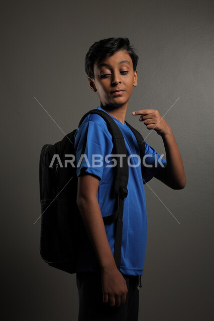 الإستعداد للعام  الجديد، الوقوف باستقامة بايماءات السعادة للعودة إلى المدارس ,  بورتريه لطالب عربي خليجي سعودي يرتدي الزي الكاجوال و يحمل الحقيبة المدرسية وينظر إلى الكاميرا ، الشعور بالحماس والنشاط ببداية السنة الدراسية ، خلفية رمادية
