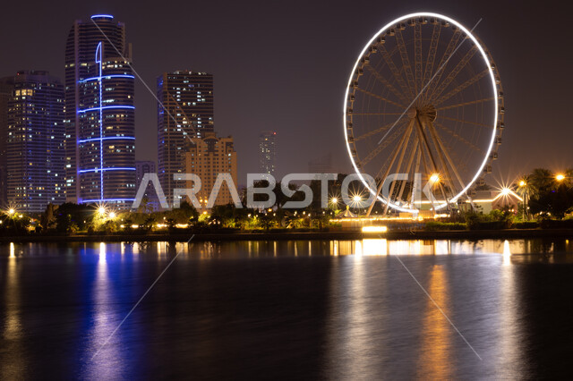 الفن الهندسي المعماري للأبراج وناطحات السحاب المضيئة ليلا المطلة على الخليج العربي، المعالم السياحية المشهورة، اماكن جذب واستقطاب السياح، اطلالة على الوجهة البحرية، كورنيش بحيرة خالد في مدينة الشارقة بالامارات العربية المتحدة