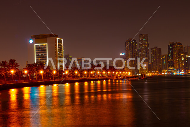 الفن الهندسي المعماري للأبراج وناطحات السحاب المضيئة ليلا المطلة على الخليج العربي، المعالم السياحية المشهورة، اماكن جذب واستقطاب السياح، اطلالة على الوجهة البحرية، كورنيش بحيرة خالد في مدينة الشارقة بالامارات العربية المتحدة