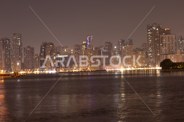 الفن الهندسي المعماري للأبراج وناطحات السحاب المضيئة ليلا المطلة على الخليج العربي، المعالم السياحية المشهورة، اماكن جذب واستقطاب السياح، اطلالة على الوجهة البحرية، كورنيش بحيرة خالد في مدينة الشارقة بالامارات العربية المتحدة