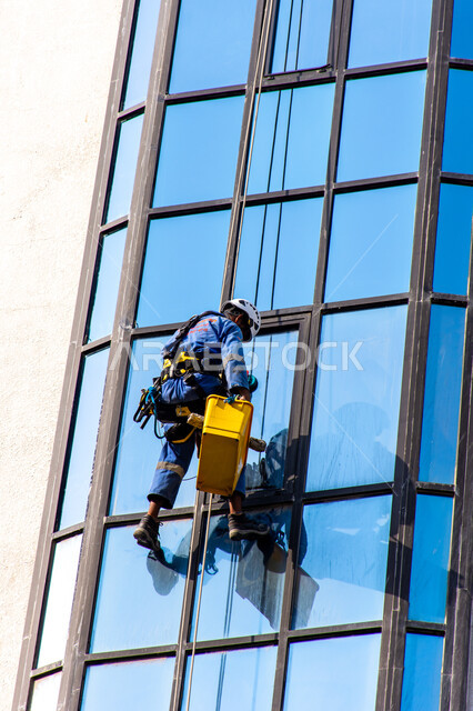 المنشآت الحديثة بديكورات وتصاميم متميزة في الإمارات العربية المتحدة، الفن الهندسي المعماري للأبراج وناطحات السحاب، عامل عربي خليجي إماراتي يقوم بتنظيف الزجاج الخارجي لبناء مرتفع شاهق، خدمة التنظيف في العمارات المرتفعة