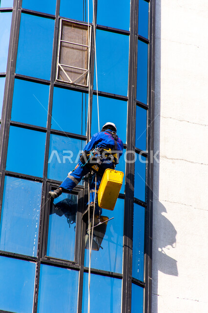 المنشآت الحديثة بديكورات وتصاميم متميزة في الإمارات العربية المتحدة، الفن الهندسي المعماري للأبراج وناطحات السحاب، عامل عربي خليجي إماراتي يقوم بتنظيف الزجاج الخارجي لبناء مرتفع شاهق، خدمة التنظيف في العمارات المرتفعة