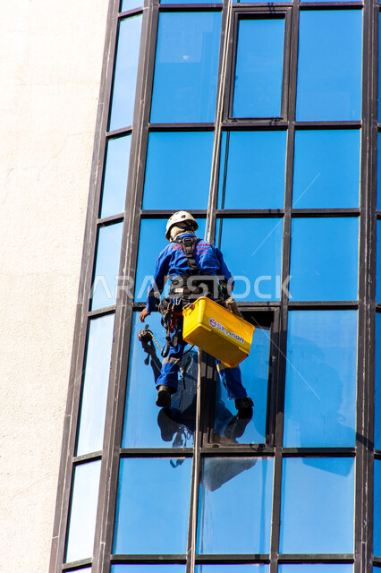 Architectural engineering art of towers and skyscrapers, modern facilities with distinctive decorations and designs in the United Arab Emirates, an Arab Gulf Emirati worker cleaning the exterior glass of a high-rise building, cleaning service in high-rise buildings