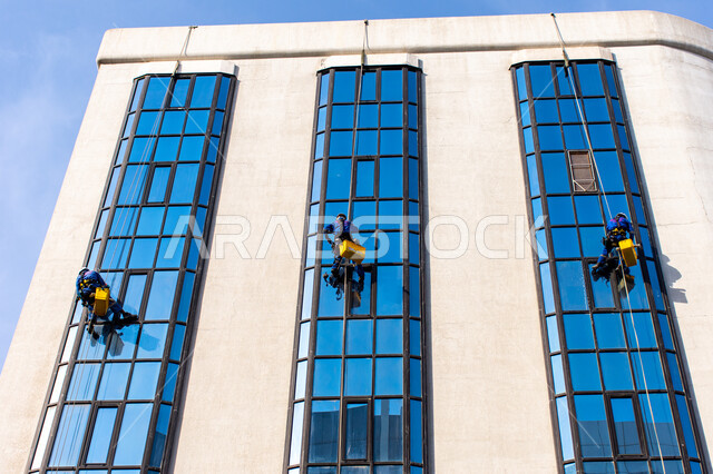 خدمة التنظيف في العمارات المرتفعة، الفن الهندسي المعماري للأبراج وناطحات السحاب، المنشآت الحديثة بديكورات وتصاميم متميزة في الإمارات العربية المتحدة، عمال عرب خليجيين إماراتيين يقومون بتنظيف الزجاج الخارجي لبناء مرتفع شاهق